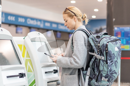 Image of Casual caucasian woman using smart phone application and check-in machine at the airport getting the boarding pass.
