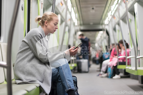 Image of Beautiful blonde woman wearing winter coat reading on the phone while traveling by metro public transport.