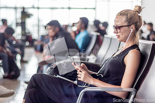 Image of Female traveler using her cell phone while waiting to board a plane at departure gates at asian airport terminal.