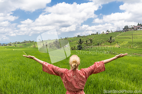Image of Relaxed fashionable caucasian woman wearing red asian style kimono, arms rised to sky, enjoying pure nature at beautiful green rice fields on Bali island