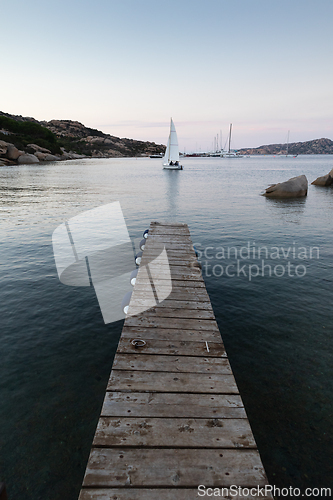 Image of Wooden pier and sailboats sailing in evening calm sea of marvellous Porto Rafael, Costa Smeralda, Sardinia, Italy. Symbol for relaxation, wealth, leisure activity