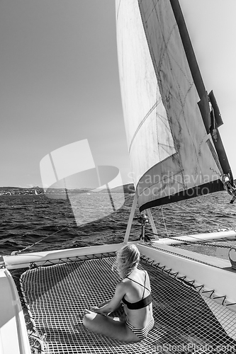 Image of Beautiful woman relaxing on a summer sailing cruise, sitting and sunbathing in hammock of luxury catamaran sailing around Maddalena Archipelago, Sardinia, Italy.