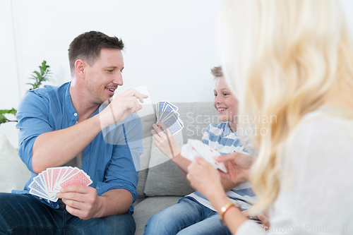Image of Happy young family playing card game at home.