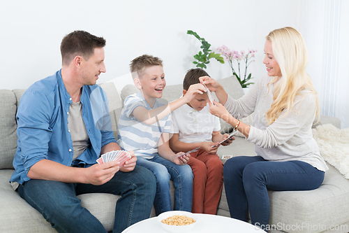 Image of Happy young family playing card game at home.
