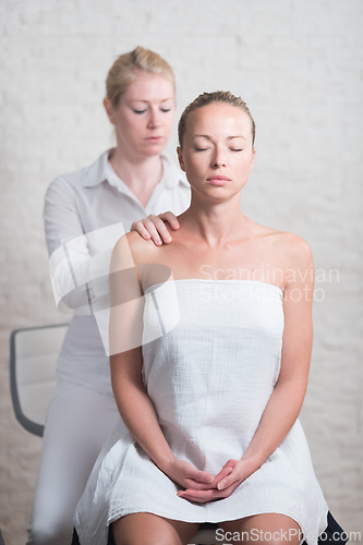 Image of Professional female masseur giving relaxing massage treatment to young female client. Hands of masseuse of neck of young lady during procedure of spa facial massage