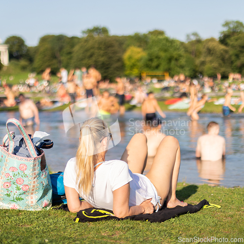 Image of People enjoying the summer, sunbathing, swimming in river Izar and relaxing on green of the Englischer Garten in Munich, Germany on a sunny summer holiday day.
