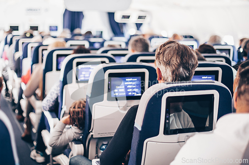 Image of Interior of airplane with passengers on seats and stewardess in uniform walking the aisle, serving people. Commercial economy flight service concept.