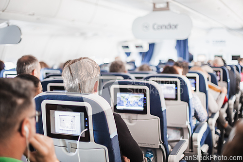 Image of Interior of airplane with passengers on seats and stewardess in uniform walking the aisle, serving people. Commercial economy flight service concept.