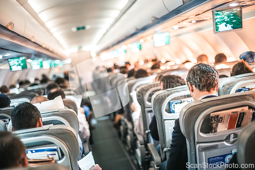 Image of Interior of airplane with passengers on seats and stewardess in uniform walking the aisle, serving people. Commercial economy flight service concept.