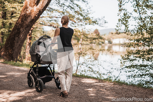 Image of Rear view of casually dressed mother walking with baby stroller in Koseski bajer city park in Ljubljana, Slovenia. Family, child and parenthood concept.