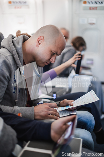 Image of Pasenger filling immigration form on flight to visit destination country sitting in airplane. Man is writing entry permit or visa on a paper on a flight. Passenger signing document on board.