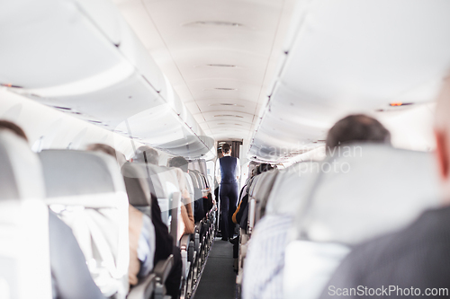 Image of Interior of airplane with passengers on seats and stewardess in uniform walking the aisle, serving people. Commercial economy flight service concept.
