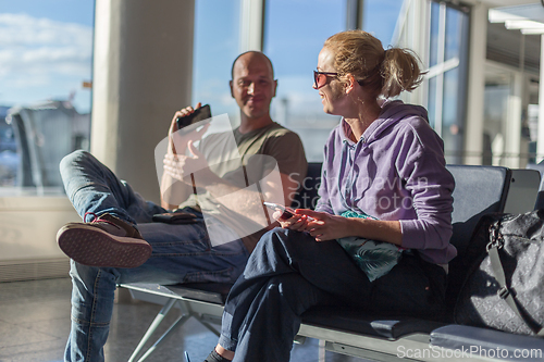 Image of Traveling couple sharing smiles on a bench at the airport, enjoying leisure time before their travel. They look happy and comfortable, having fun together.