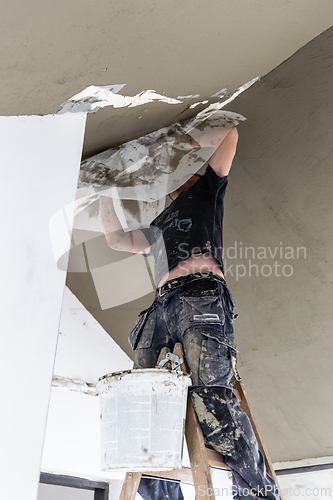Image of Male builder at work overalls plastering and restoring old wall using a construction trowel