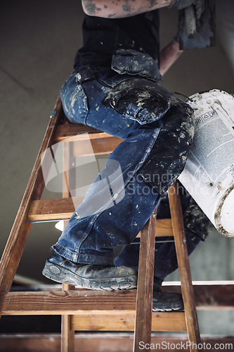 Image of Male builder at work overalls plastering and restoring old wall using a construction trowel