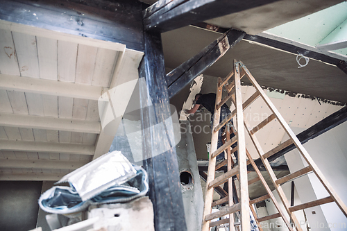 Image of Male builder at work overalls plastering and restoring old wall using a construction trowel