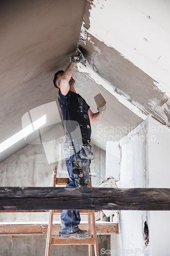 Image of Male builder at work overalls plastering and restoring old wall using a construction trowel