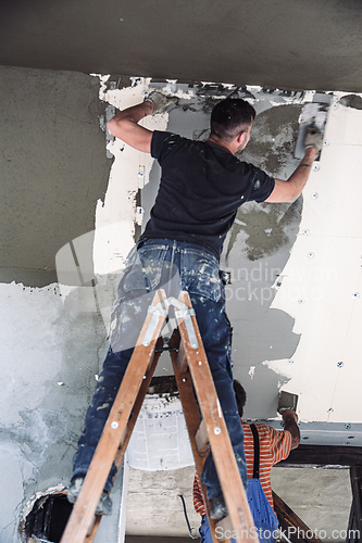 Image of Male builder at work overalls plastering and restoring old wall using a construction trowel