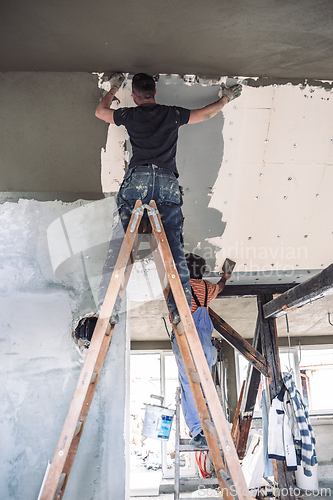 Image of Male builder at work overalls plastering and restoring old wall using a construction trowel