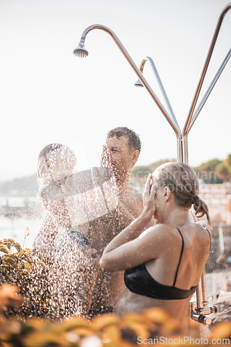Image of Mom, dad and their toddler child under a tropical shower. Parents with their cute infant boy playing on the beach under shower water splashes. Playful moment at summer family holiday.