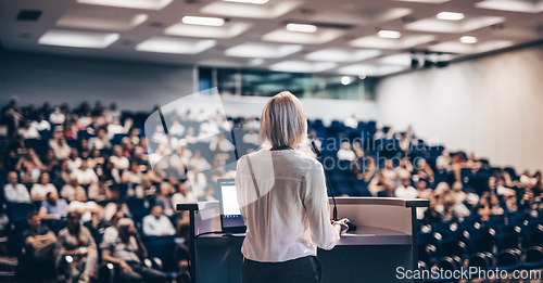 Image of Female speaker giving a talk on corporate business conference. Unrecognizable people in audience at conference hall. Business and Entrepreneurship event.