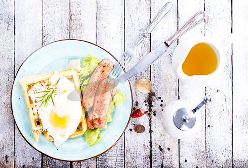Image of Delicious breakfast. Served on a wooden table with toast, eggs, sausage, wafers, juice.
