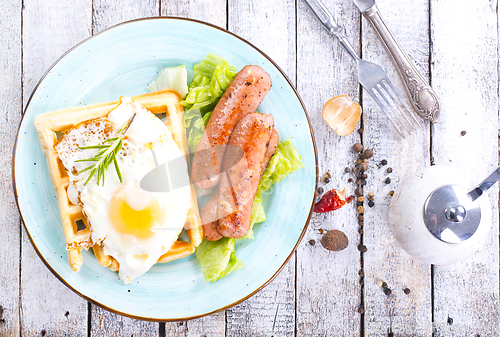 Image of Delicious breakfast. Served on a wooden table with toast, eggs, sausage, wafers, juice.