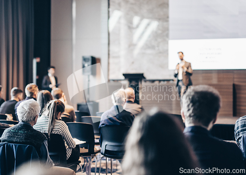 Image of Speaker giving a talk in conference hall at business event. Rear view of unrecognizable people in audience at the conference hall. Business and entrepreneurship concept.