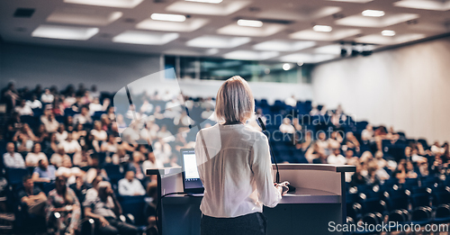 Image of Female speaker giving a talk on corporate business conference. Unrecognizable people in audience at conference hall. Business and Entrepreneurship event.