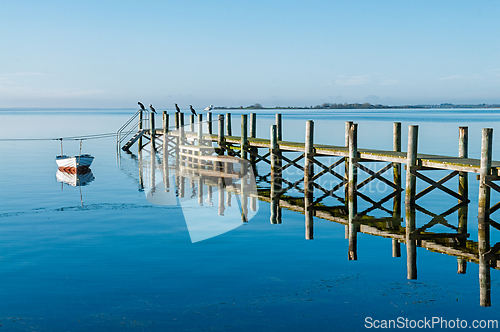 Image of Serene dock reflects in calm water with a small boat moored in a
