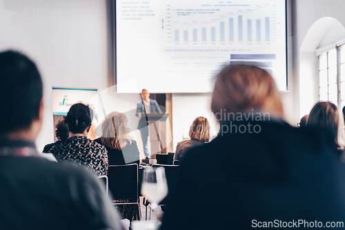 Image of Speaker giving a talk in conference hall at business event. Rear view of unrecognizable people in audience at the conference hall. Business and entrepreneurship concept.