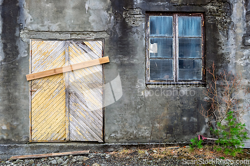 Image of Old abandoned building with boarded door and cracked window in a