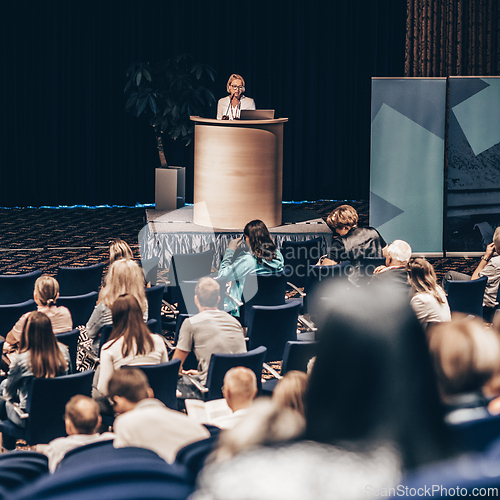 Image of Female speaker giving a talk on corporate business conference. Unrecognizable people in audience at conference hall. Business and Entrepreneurship event.