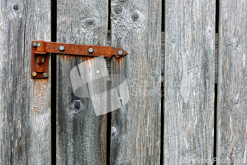 Image of Rusty hinge on weathered wooden door in rural setting during day