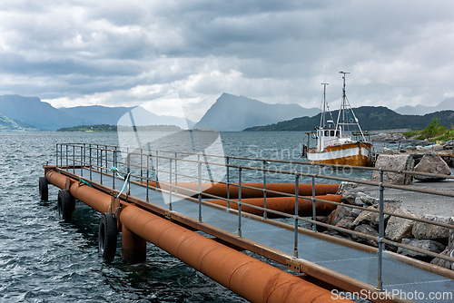 Image of Fishing boat docked at a pier surrounded by mountains and cloudy