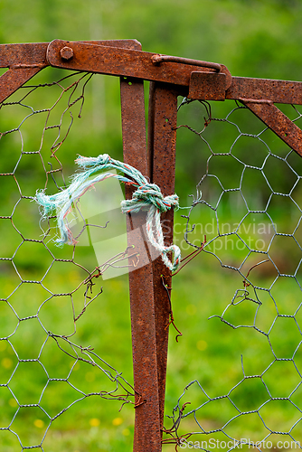 Image of Rusty gate secured with blue rope in a lush green field during s
