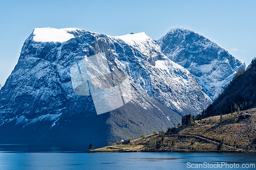 Image of Snow-capped mountains rise above a tranquil fjord under a clear 