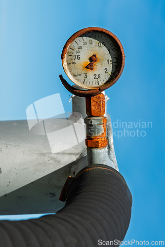Image of Rusty pressure gauge mounted on a pipeline under a clear blue sk