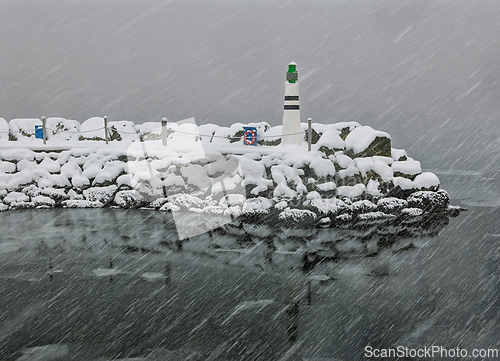 Image of Snow covered pier and lighthouse during a winter storm near a tr