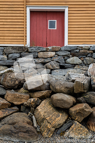 Image of Sturdy stone wall supporting a rustic orange barn with a red doo