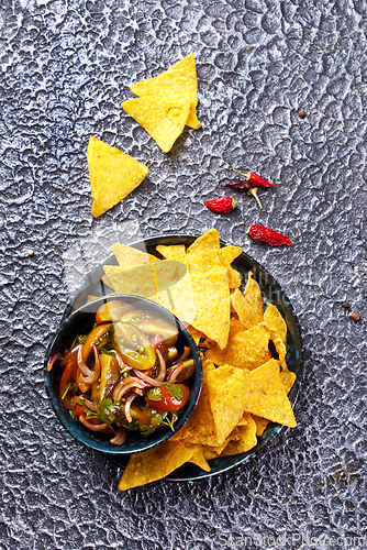 Image of Single big black plate of yellow corn tortilla nachos chips with salsa sauce