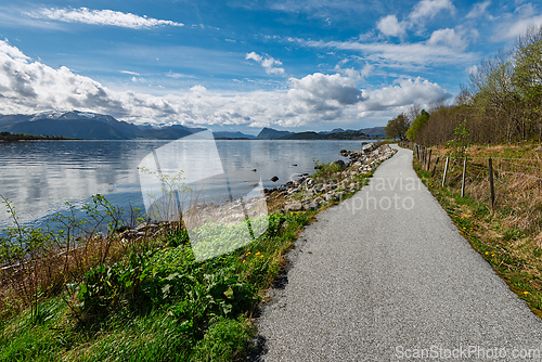 Image of Scenic waterfront path in a serene landscape with mountains and 