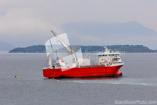 Image of Large red supply vessel navigating calm waters near an island in