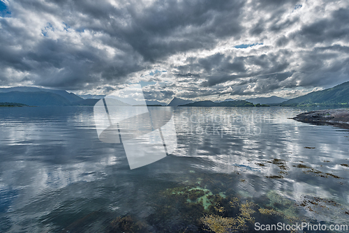 Image of Calm waters reflect dramatic clouds over a serene landscape at t