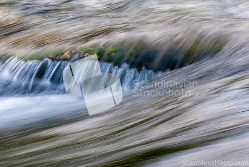 Image of Water flowing over smooth rocks in a serene stream during daylig