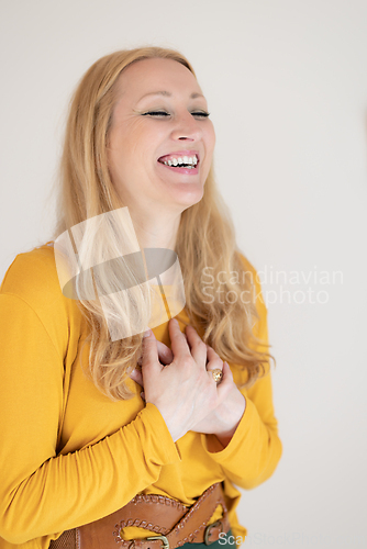 Image of Portrait of cheerful confident beautiful woman with long blond hair, wearing casual clothes, standing in relaxed pose with hands on chest, breathing deeply, doing breathing exercise