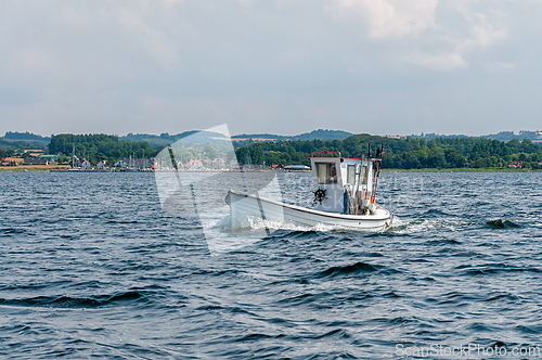 Image of White fishing boat gliding through calm waters near coastal town