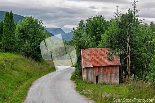 Image of Rustic shed sits beside a winding road surrounded by lush greene