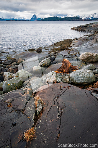 Image of Rocky shoreline by the sea with distant mountains and overcast s