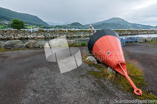Image of Large buoy sits on rocky shore against backdrop of mountains and